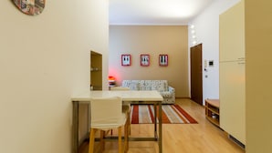 Un ambiente compatto con angolo pranzo, un divano a fantasia e una piccola cucina.