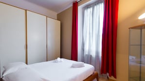 Un letto rifatto con lenzuola bianche e asciugamani arrotolati, una testiera in legno e un ampio armadio con ante scorrevoli.