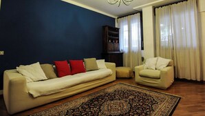 A living room with a sofa, a chair, a rug, a chandelier, and a bookshelf. - Park Apartment (Milan)