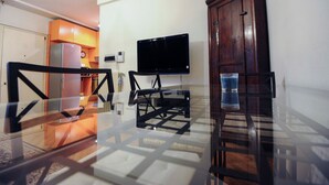 A living room with a glass coffee table, a wooden cabinet, a flat-screen TV, and a glass of blue liquid on the table. - Park Apartment (Milan)