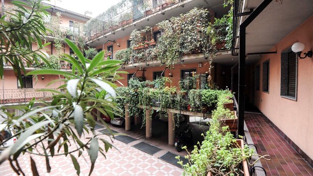 A courtyard with potted plants, a scooter, and a tiled floor. - Park Apartment (Milan)