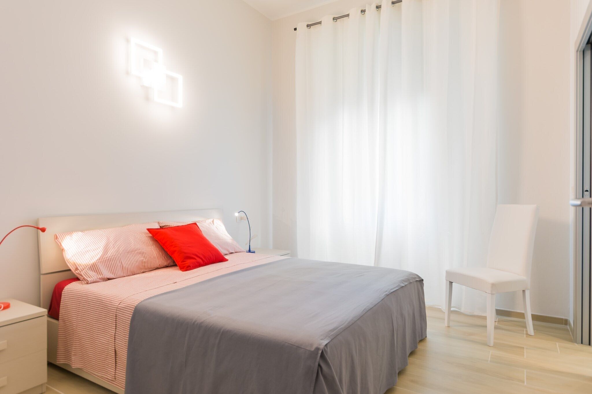 A modern bedroom with a bed, a chair, a nightstand, and a wall-mounted light fixture.
