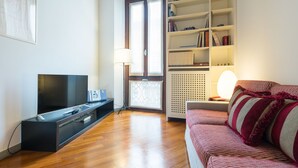 Una sala de estar con televisor de pantalla plana, un sofá, una estantería y un radiador.