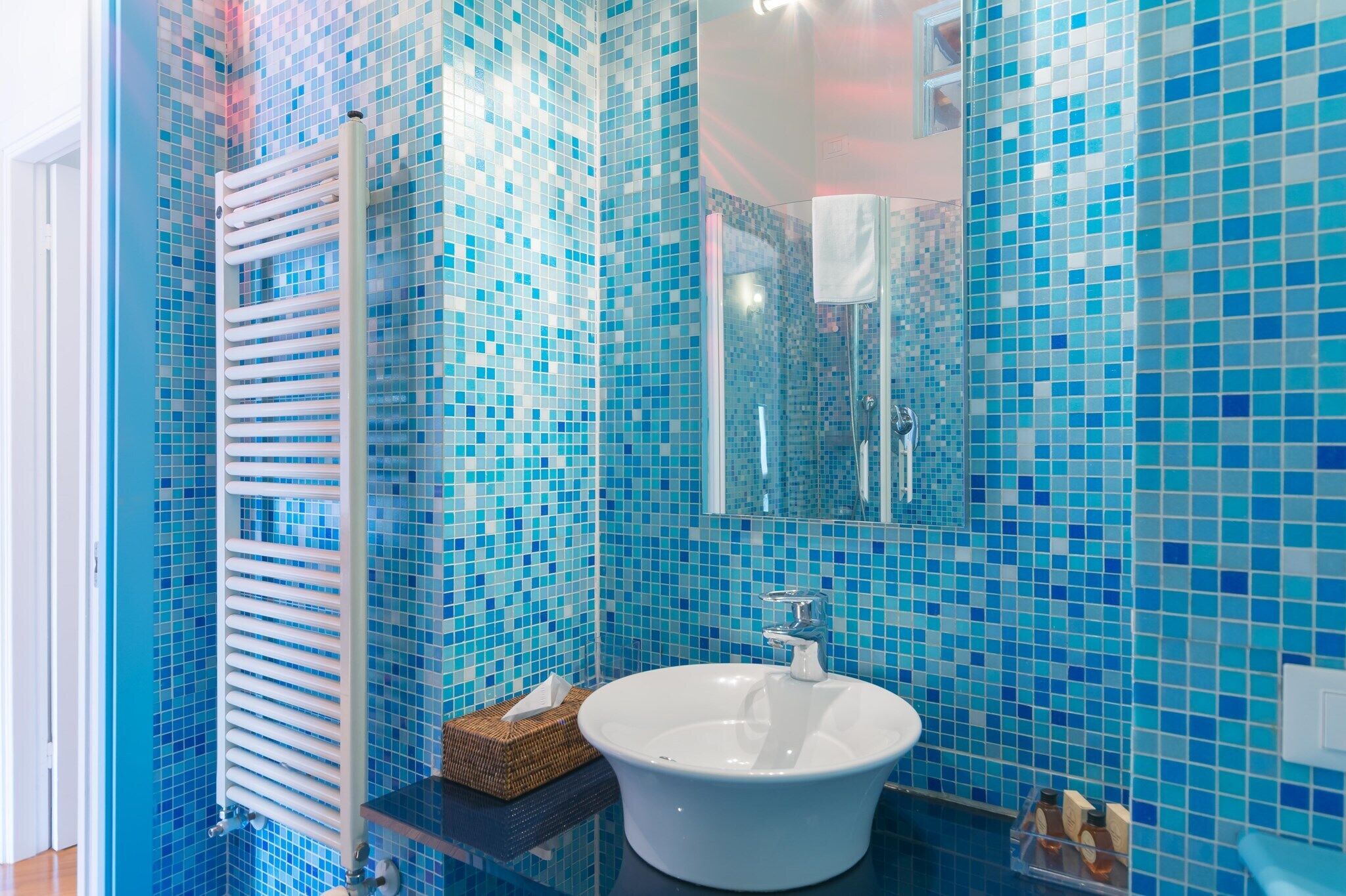 A bathroom with a white sink, blue mosaic tiles, a towel rack, and a mirror.