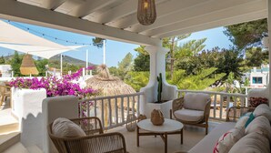 A covered outdoor seating area with wicker furniture, a round table, and a decorative plant. - Villa Clara Ibiza with pool (Santa Eulària des Riu)