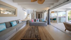 A modern living room with a grey sofa, a wooden coffee table, and a ceiling fan. - Villa Clara Ibiza with pool (Santa Eulària des Riu)