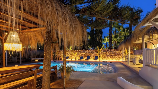 A pool area with lounge chairs, a wooden deck, and a thatched roof structure. - Villa Clara Ibiza with pool (Santa Eulària des Riu)