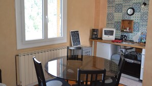 A compact kitchen with a dining table, chairs, a coffee maker, a microwave, and a patterned backsplash.