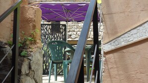A narrow outdoor corridor with a stone wall, a green chair, and a purple umbrella.