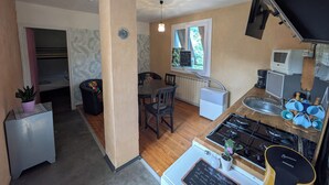 A compact kitchen with a gas stove, a microwave, and a sink. There is a dining table with chairs, a small refrigerator, and a potted plant.