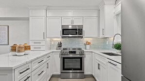 A modern kitchen with white cabinetry, a stainless steel oven, a microwave, and a sink. - Stunning Gulf Front Townhouse! Private beach, beach chairs, wagon, and cooler! (Santa Rosa Beach)