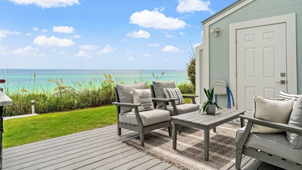 A deck with outdoor furniture, a view of the ocean, and a building with a door. - Stunning Gulf Front Townhouse! Private beach, beach chairs, wagon, and cooler! (Santa Rosa Beach)