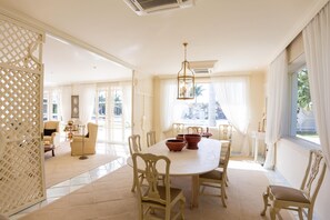 A spacious dining area with a round table, white chairs, and a decorative chandelier.