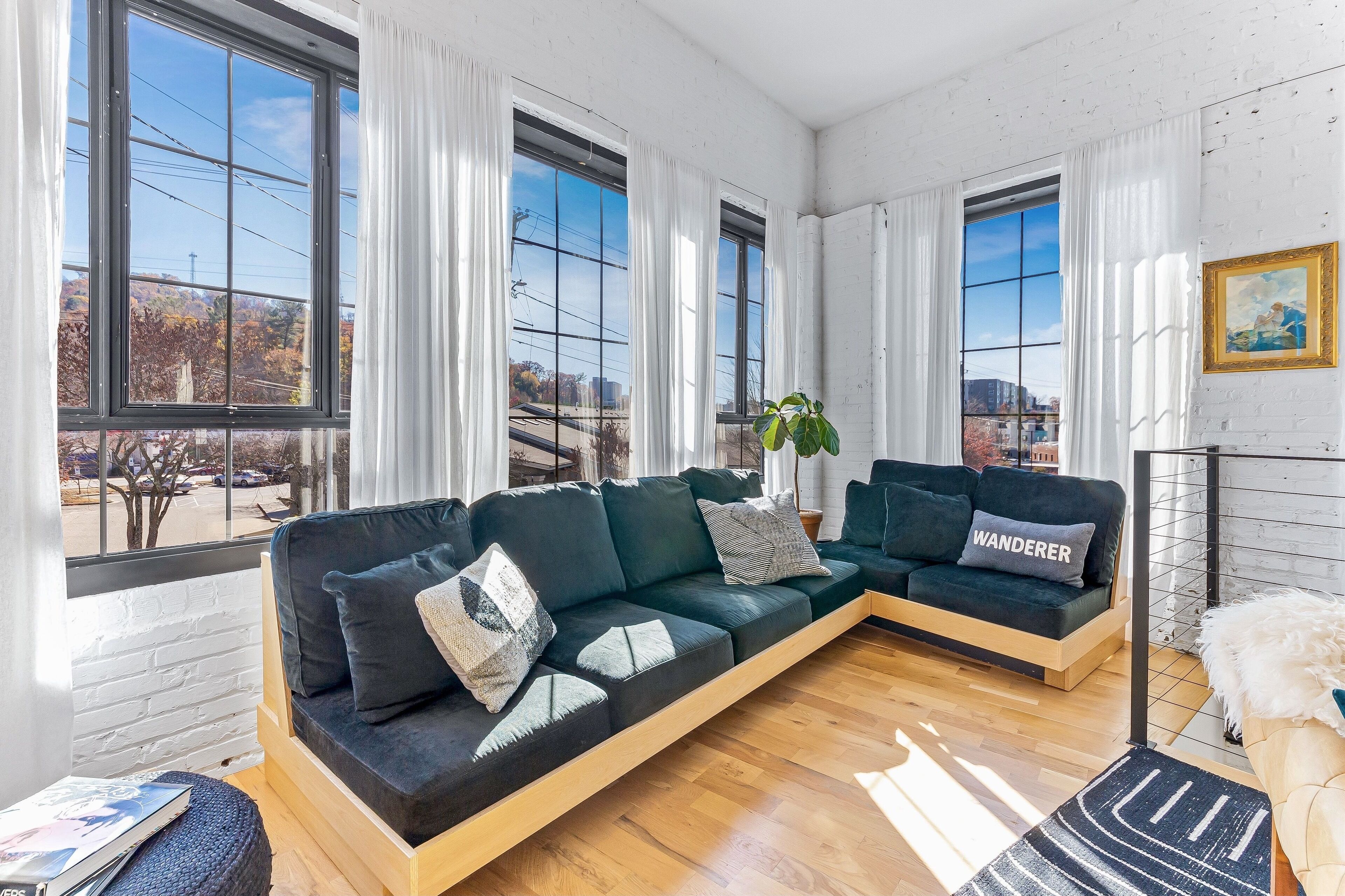 Un salon moderne avec un canapé d’angle, de grandes fenêtres et une vue sur la ville.