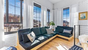 Un salon moderne avec un canapé d’angle, de grandes fenêtres et une vue sur la ville.