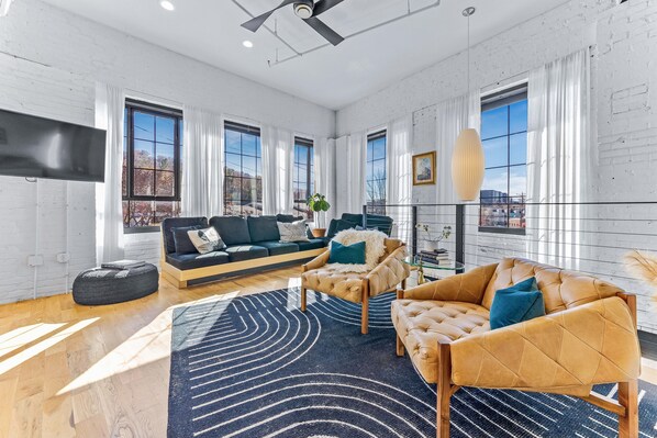 A spacious living room with a modern sofa set, a large black rug, and a view of the city through large windows.