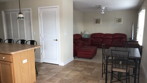 Una cocina con una isla de madera, zona de comedor con una mesa y sillas, un sofá rojo y un ventilador de techo.