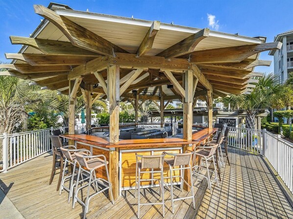 A wooden deck with a bar area, outdoor seating, and a view of the surrounding buildings.