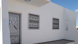A white building with a geometric patterned door, two decorative windows, and a small set of steps leading to a tiled entrance.