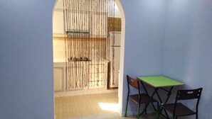 A room with a dining table and chairs, an arched doorway leading to a kitchen, and a light-colored floor.