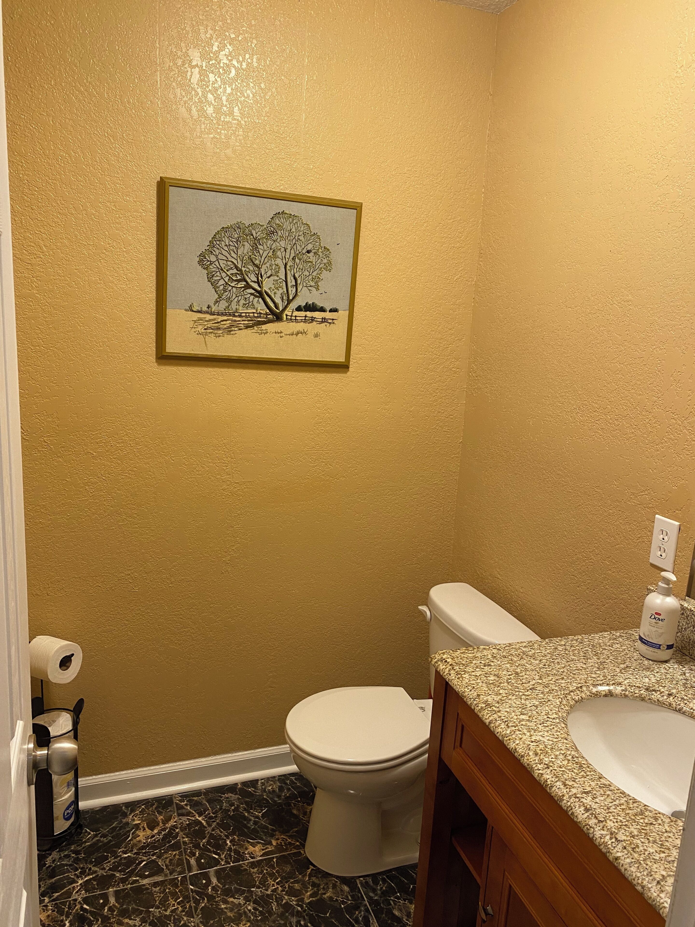Une salle de bain avec des toilettes, un lavabo, un sol en marbre et un tableau encadré au mur.