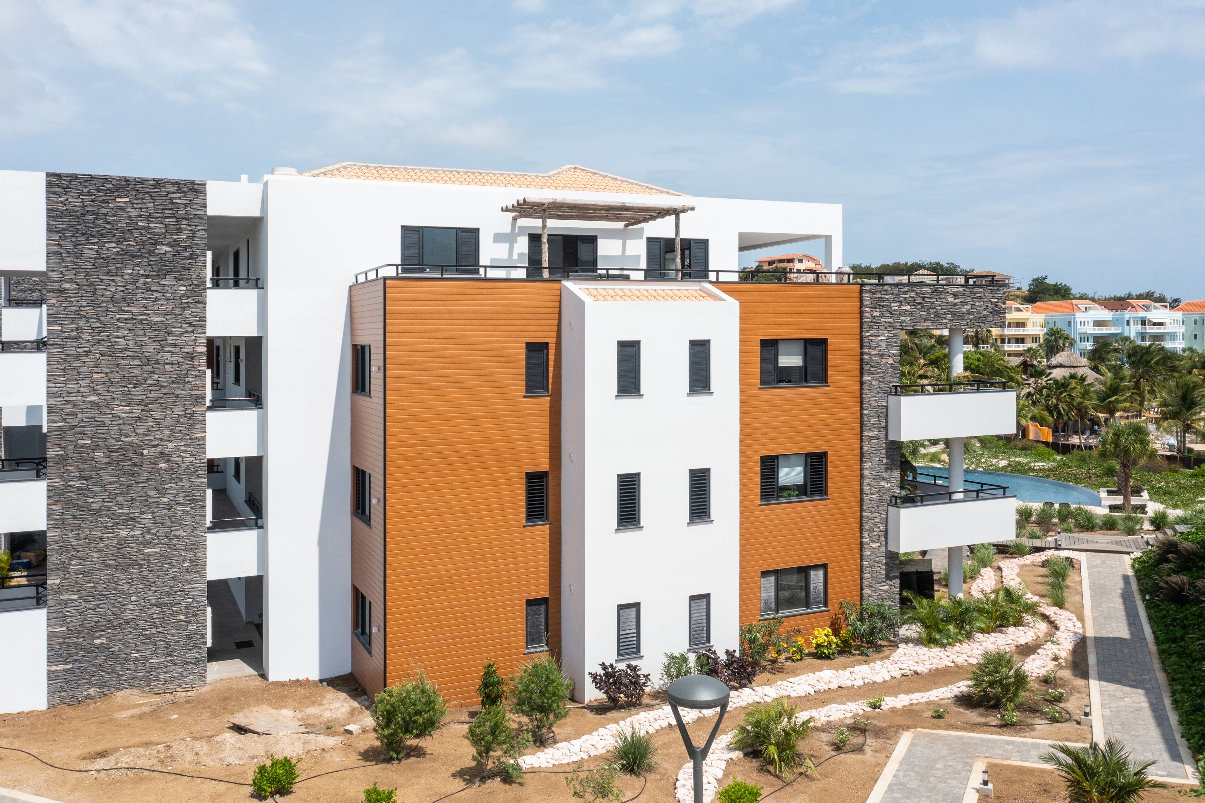 Un hôtel moderne à plusieurs étages, dont la façade est un mélange de pierre et de bois, doté de balcons et d’un espace piscine.