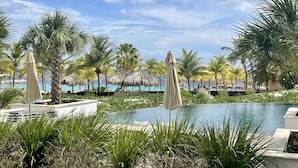 A pool area with palm trees, umbrellas, and a view of the ocean.