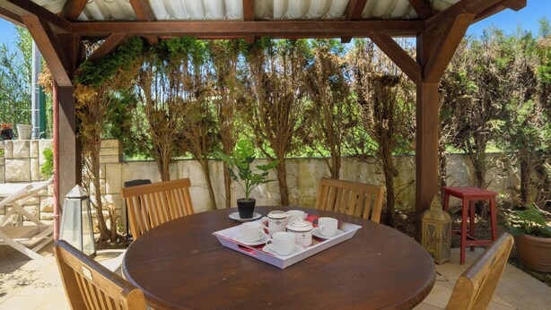 An outdoor wooden table with chairs, a tray with cups and a teapot, surrounded by greenery and a stone wall. - Charming Apartment with Garden - beach 300 m away (Vinkuran)