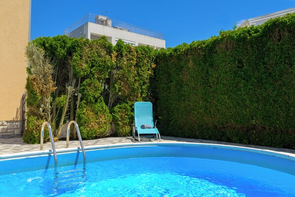 A swimming pool with a blue chair and a ladder, surrounded by greenery and a building in the background. - Charming Apartment with Garden - beach 300 m away (Vinkuran)