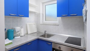 A compact kitchen with blue cabinets, a stainless steel sink, and a window above the countertop. - Charming Apartment with Garden - beach 300 m away (Vinkuran)
