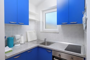 Eine kleine Küche mit blauen Schränken, einer Edelstahl-Spüle und einem Fenster über der Arbeitsfläche.