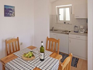 A small kitchen with a dining table set for two, a bottle of wine, and a bowl of fruit.