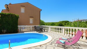 A swimming pool with a tiled deck, lounge chairs, and a building in the background. - Charming Apartment with Garden - beach 300 m away (Vinkuran)
