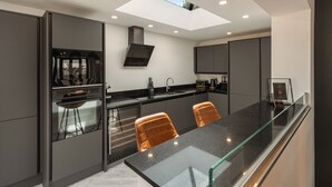 A modern kitchen with a glass-top dining table, dark cabinetry, and a skylight. - No3 Highpoint luxury townhouse, 2en-suite bedrooms onsite indoor swimming pool  (Saundersfoot)