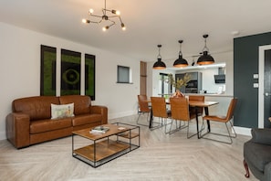 Una sala de estar moderna con un sofá de cuero marrón, una mesa de centro de madera y una zona de comedor con una mesa y sillas.