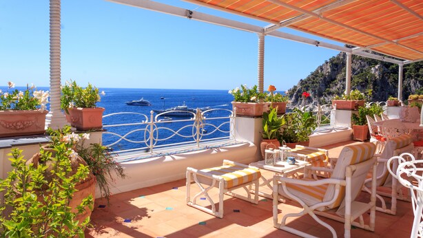 A terrace with outdoor seating, potted plants, and a view of the sea. - Villa Faraglioni Capri (Capri)