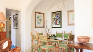 A dining area with a glass-top table, green upholstered chairs, and a large terracotta bowl. - Villa Faraglioni Capri (Capri)