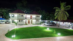 A two-story building with a flat roof, a well-maintained lawn, and several parked cars. - Naf Apartments - Mtwara (Mtwara)