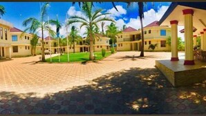 A courtyard with palm trees, a covered seating area, and a building with a red roof. - Naf Apartments - Mtwara (Mtwara)