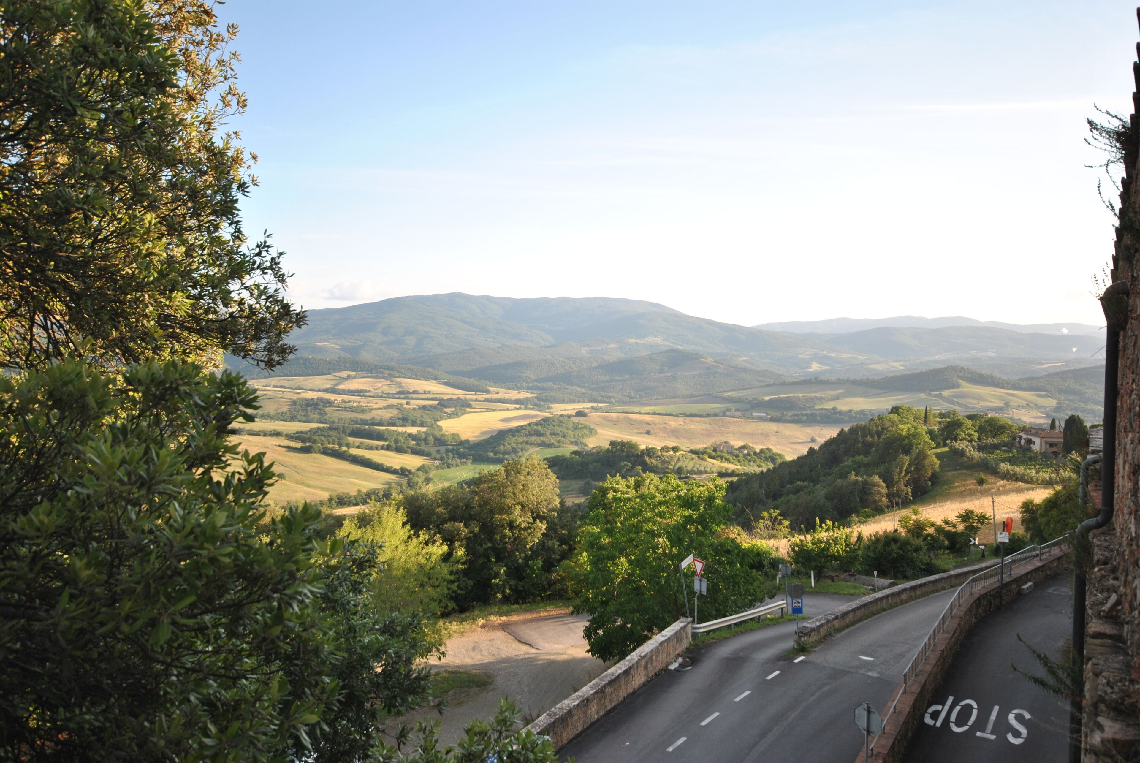 Una carretera serpentea por un paisaje montañoso, con una señal de stop y un muro de piedra a la derecha.