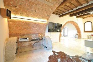 Une pièce avec un mur en briques, un téléviseur à écran plat fixé au mur, une cheminée en pierre et une sculpture en pierre posée sur le sol.