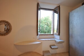 Une salle de bain avec un grand lavabo, une fenêtre donnant sur les arbres et un miroir au mur.