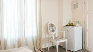 Ein Zimmer mit einem Bett, einem Sessel, einem kleinen, weißen Kühlschrank und einer Tür.