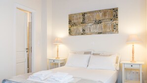 Ein ordentlich bezogenes Bett mit gefalteten weißen Handtüchern, zwei Nachttische mit Lampen und ein dekoratives Wandbild darüber.