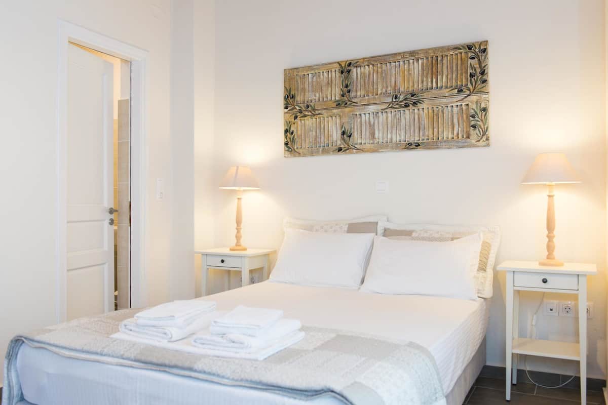 A neatly made bed with folded white towels, two bedside tables with lamps, and a decorative wall piece above the bed.