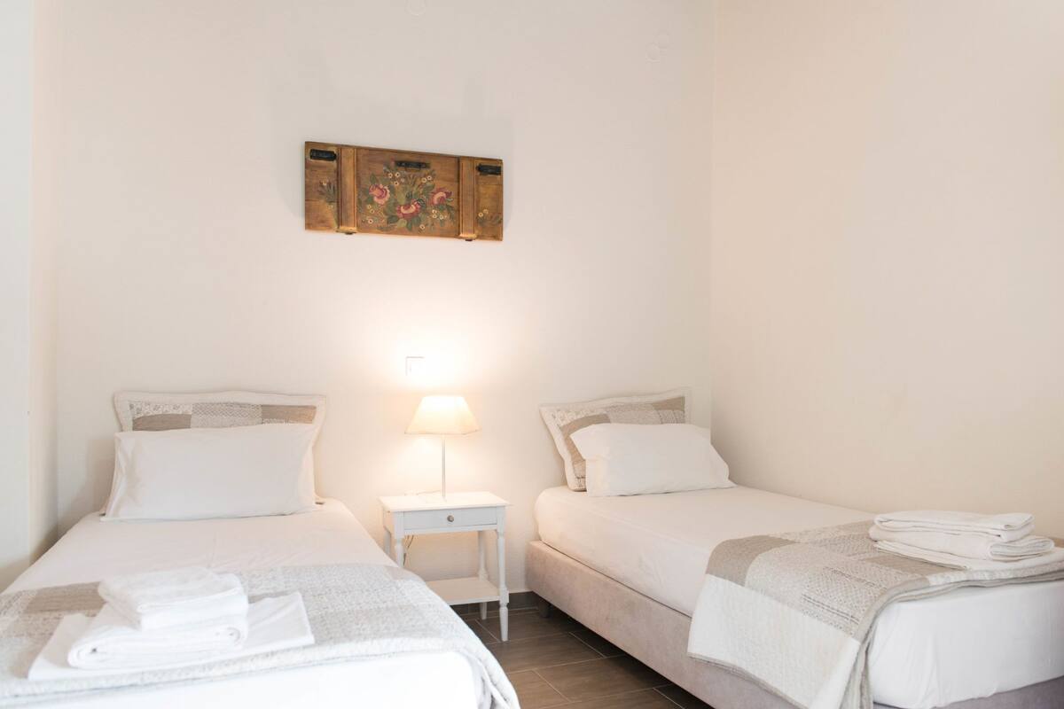 A twin room with two beds, a nightstand with a lamp, and a wall-mounted artwork.