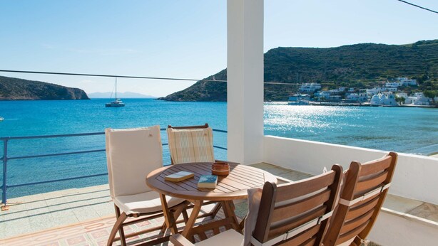 Ein Balkon mit Tisch und Stühlen und Blick auf die Küste, wo Boote und Gebäude zu sehen sind.