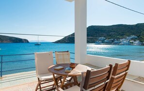 A balcony with a table and chairs overlooking a coastal view with boats and buildings. - Aerides Rooms (Sifnos)
