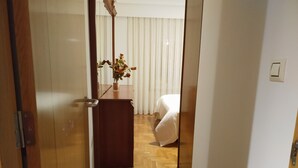 A hotel room with a wooden floor, a bed, a nightstand with a vase of flowers, and a window with white curtains. - Anjelus apartment in Mutriku (Mutriku)