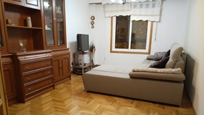 A living room with a sofa, wooden cabinet, television, and a window with curtains. - Anjelus apartment in Mutriku (Mutriku)